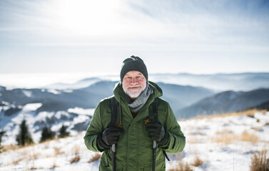 Portrait of senior man standing in snow-covered winter nature, looking at camera.