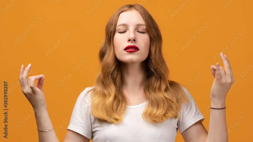Young pretty woman with wavy redhead keeps hands in mudra gesture, holds fingers in yoga sign Young pretty woman with wavy redhead keeps hands in mudra gesture, holds fingers in yoga sign