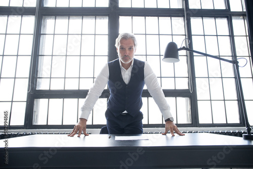 Obraz na plátne Confident businessman posing leaning on a table in an office