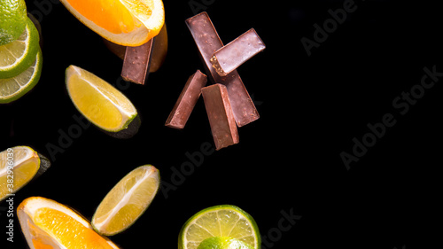 Fresh lemon lime orange slices with chocolate pieces on a black background top view