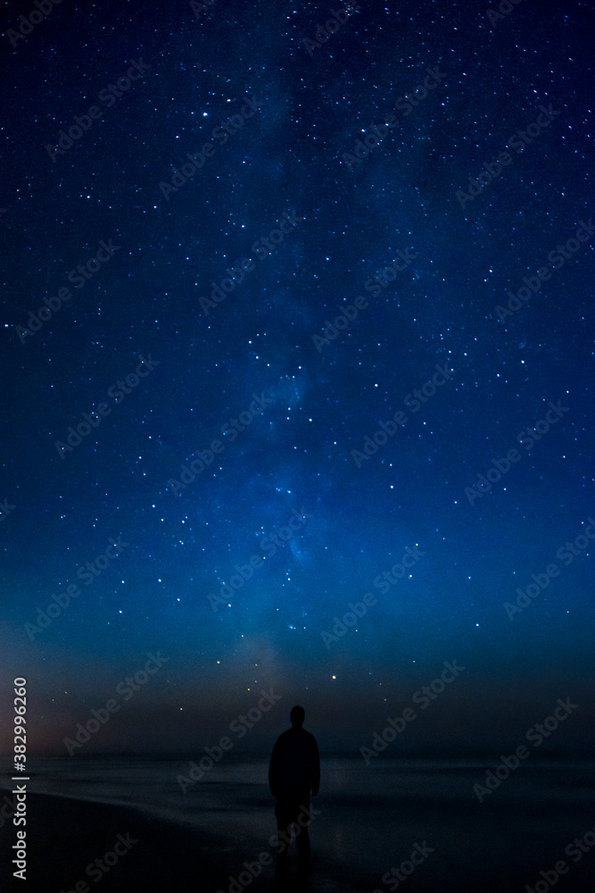 Fototapeta premium Adventurous man watching the stars on a beach at night. 