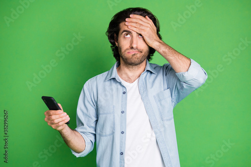 Portrait of his he nice attractive unsure depressed clueless guy using device browsing post news face palm don't know isolated over bright vivid shine vibrant green color background