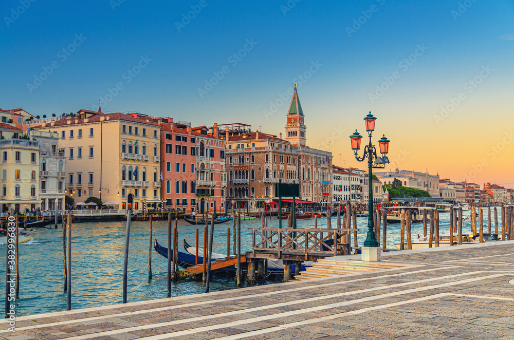 Venice evening view with Fondamenta Salute embankment promenade near pier of Grand Canal waterway at sunset, Campanile bell tower and row of baroque style buildings in San Marco sestiere, Italy