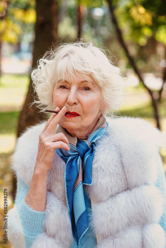 sad fashionable senior woman with grey hair in fur coat outdoor smoking cigarette. Unhealthy lifestyle, age, oldness, addiction, bad habit concept. sad fashionable senior woman with grey hair in fur coat outdoor smoking cigarette. Unhealthy lifestyle, age, oldness, addiction, bad habit concept.