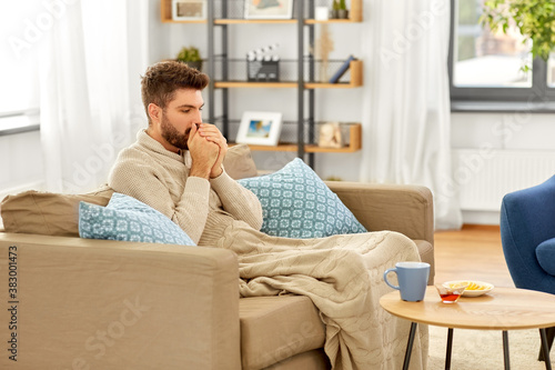 health, cold and people concept - sick young man in blanket with hot tea, lemon and honey on table at home