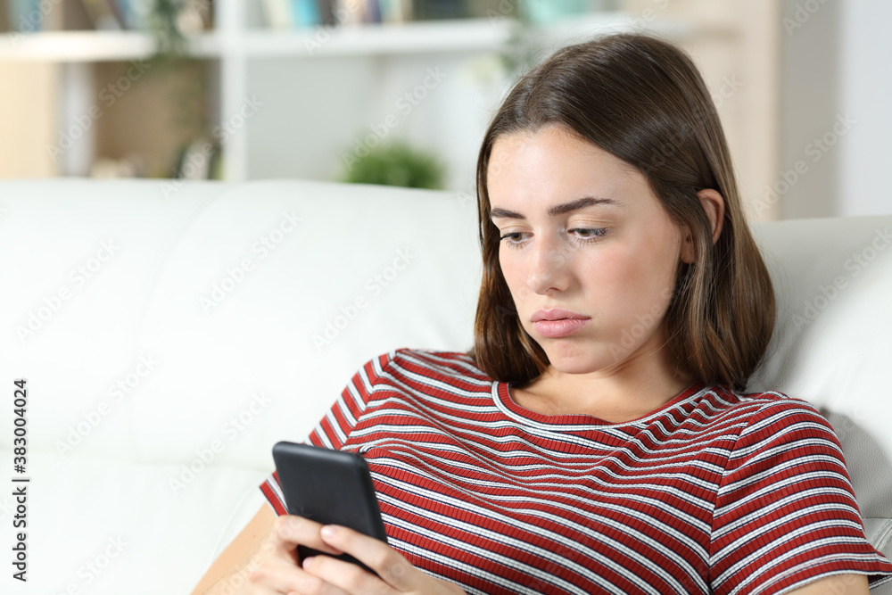 Bored teen checking smart phone on a sofa Bored teen checking smart phone on a sofa
