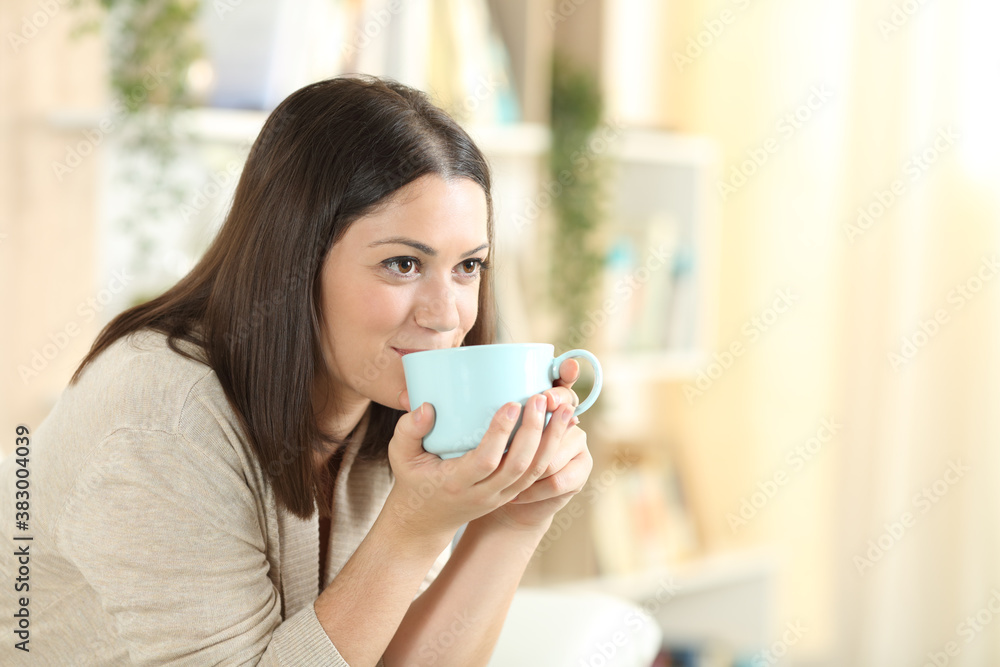 Happy woman drinking coffee sitting on a sofa at home Happy woman drinking coffee sitting on a sofa at home