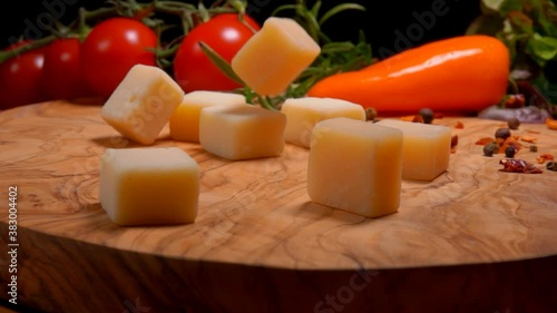 Hard cheese cubes are falling and bouncing on a wooden board on the background of spices and tomatoes photo