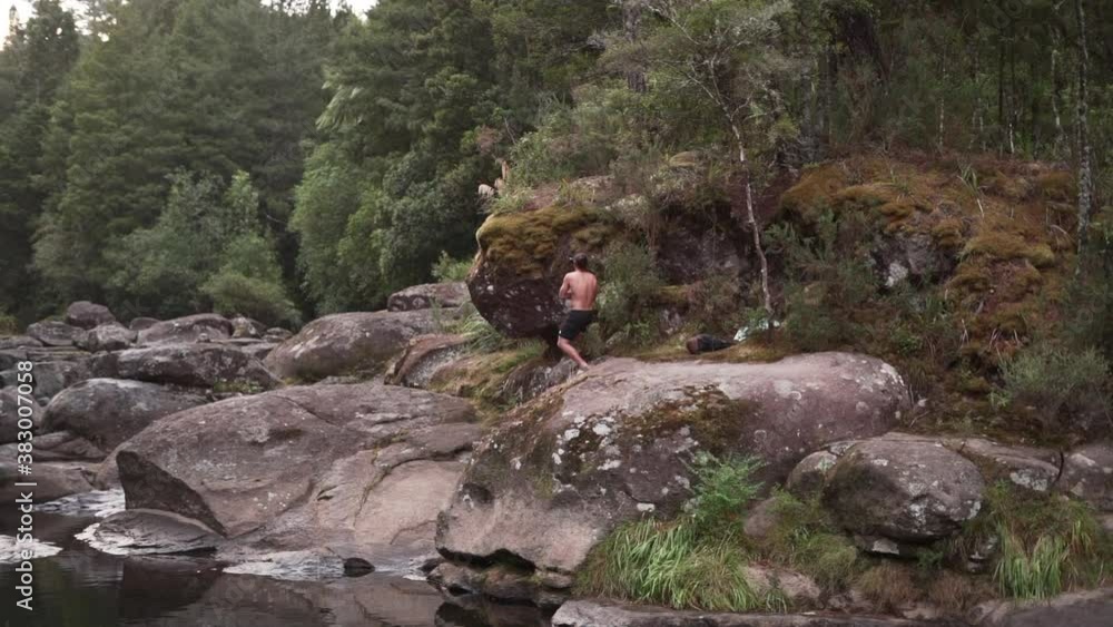 Young bare-chested man stands on cliff with camera in New Zealand