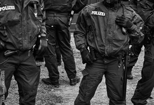 Policemen in black uniforms with pistols, handcuffs and batons, black and white, inscription Pollizei translates Police