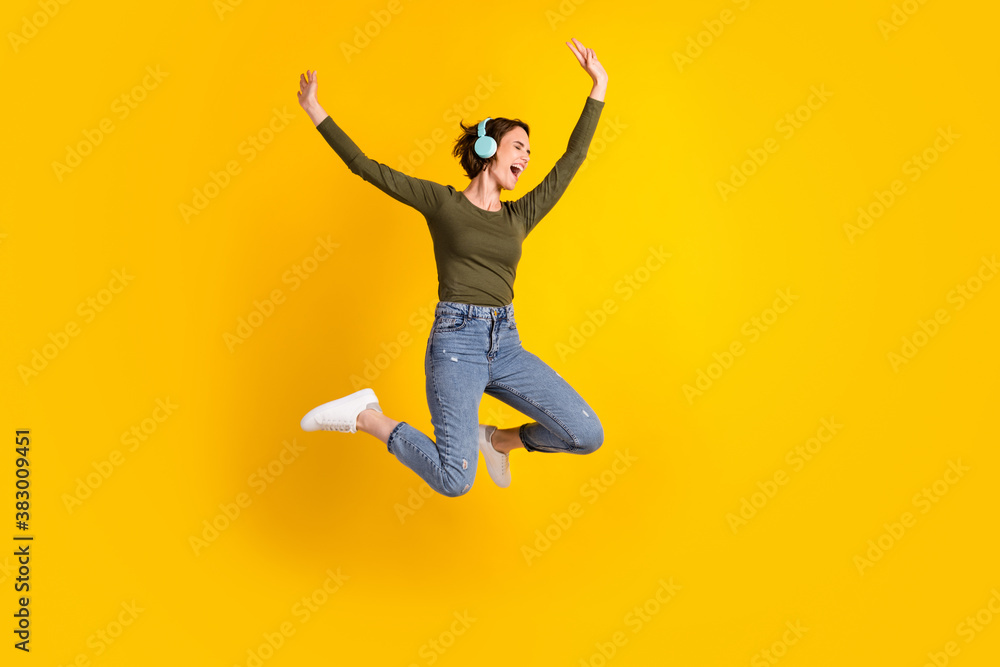 Full size photo of crazy excited girl jump listen wireless headset isolated over bright yellow color background Full size photo of crazy excited girl jump listen wireless headset isolated over bright yellow color background