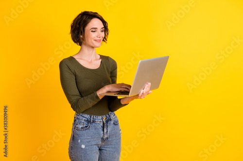 Photo of positive lady chatting on laptop wear green sweater isolated over bright yellow color background