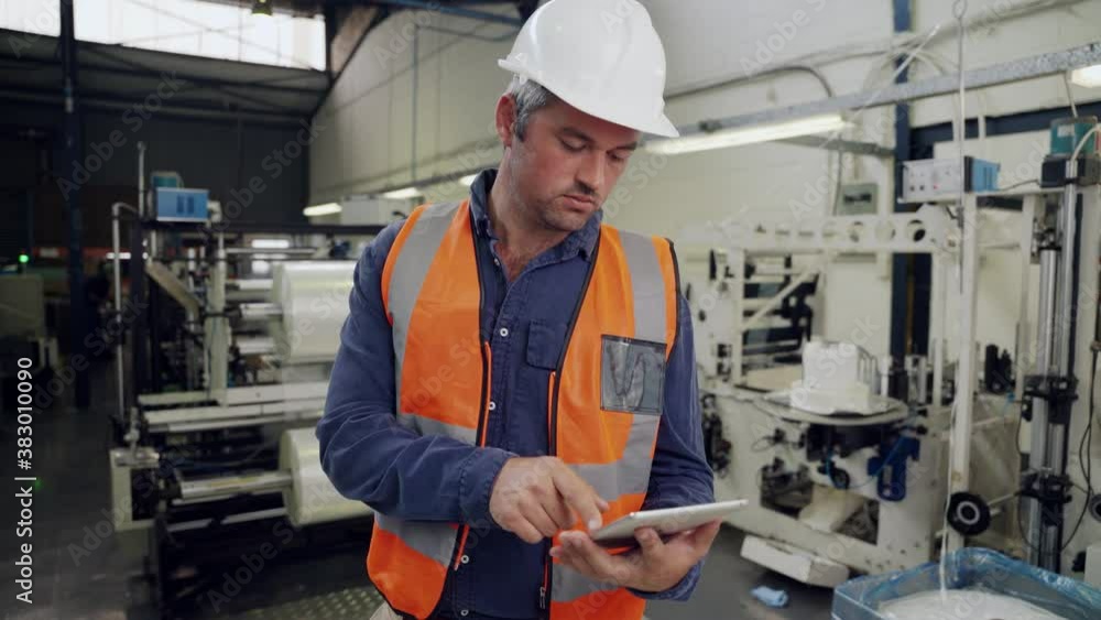 Male business man scrolling through emails on digital tablet chatting to manager standing in factory Male business man scrolling through emails on digital tablet chatting to manager standing in factory