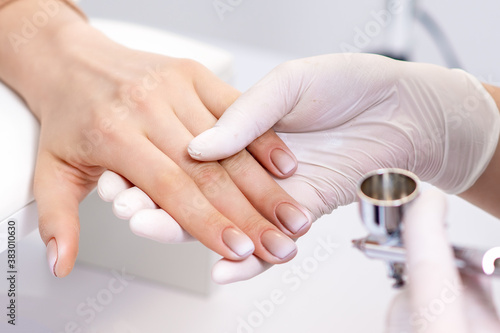 Young woman receiving manicure by airbrush in nail salon. Procedure for spraying paint on the nails