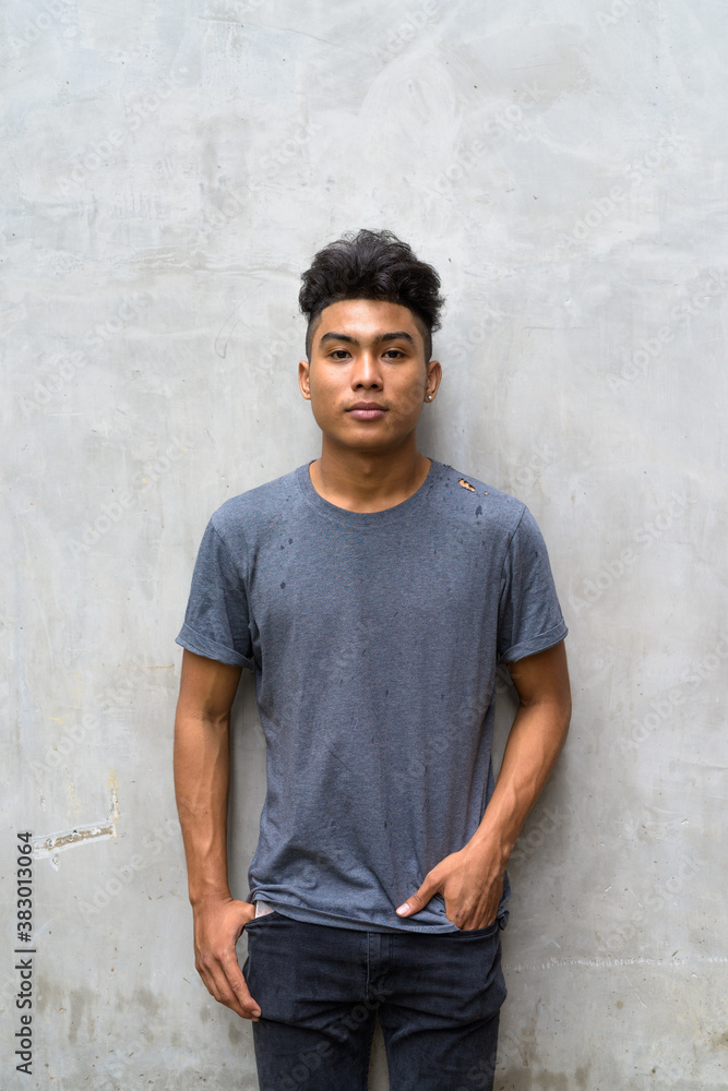 Young Asian man with curly hair against concrete wall outdoors Young Asian man with curly hair against concrete wall outdoors