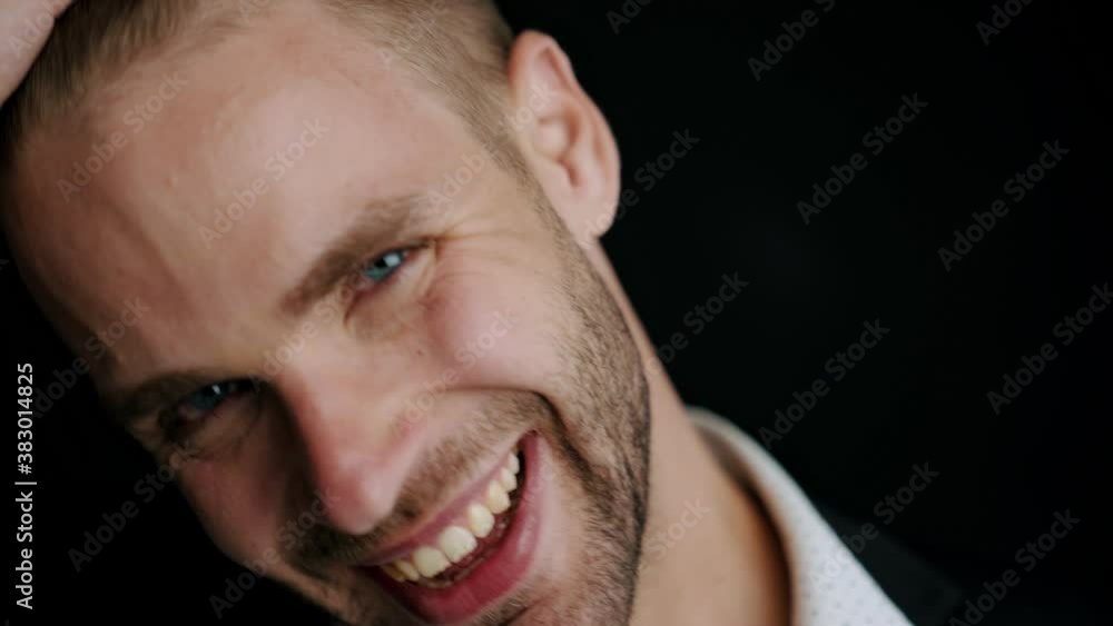 A close-up view of a happy young man is rejoicing while touching his hairstyle and looking to the camera standing isolated over black background A close-up view of a happy young man is rejoicing while touching his hairstyle and looking to the camera standing isolated over black background