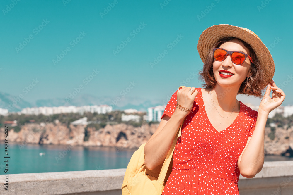 An attractive woman in a straw hat and red dress relaxes and admires the views of the Mediterranean sea resort and Riviera. Travel and vacation concept