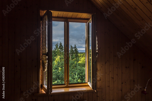 Summer in the village. Early morning . Scenic view from the window to the sky and trees. Room in the attic, with wooden siding.