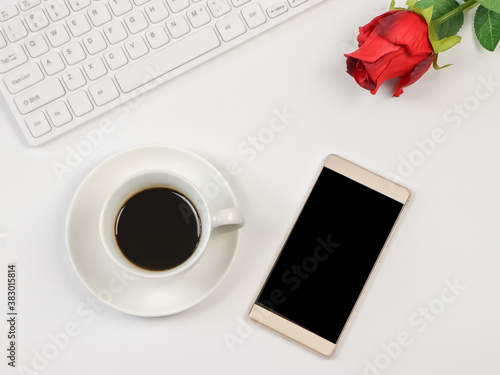 flat lay of mobile phone, coffee cup, computer keyboard and red rose  on white background . Positive morning routine, online dating and valentine's concept.