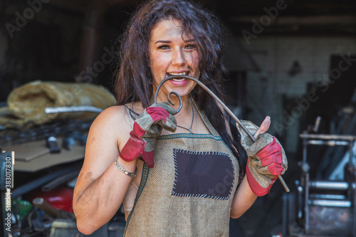 beautiful girl blacksmith bites a curved metal rod