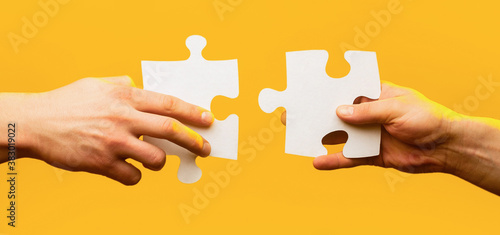 Two hands trying to connect couple puzzle piece on yellow background. Teamwork concept. Holding puzzle. Closeup hand of connecting jigsaw puzzle. Business solutions, success and strategy concept