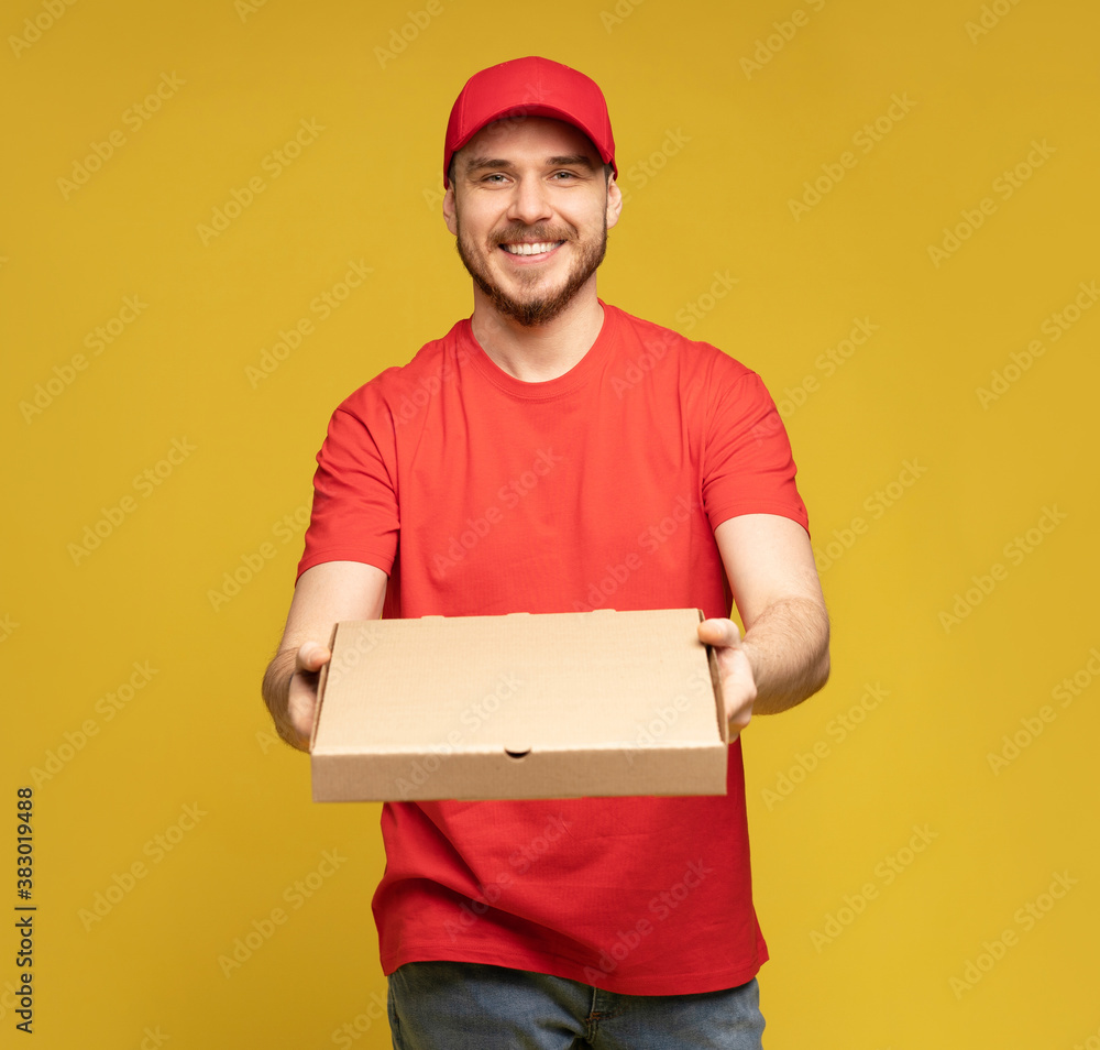 Photo of happy man from delivery service in red t-shirt and cap giving food order and holding pizza box isolated over yellow background Photo of happy man from delivery service in red t-shirt and cap giving food order and holding pizza box isolated over yellow background