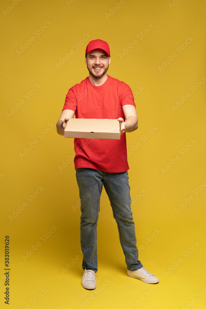 Photo of happy man from delivery service in red t-shirt and cap giving food order and holding pizza box isolated over yellow background Photo of happy man from delivery service in red t-shirt and cap giving food order and holding pizza box isolated over yellow background