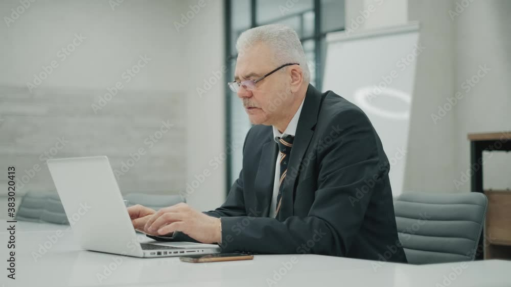 Professional matured entrepreneur reading financial news browsing web page on laptop computer doing remote job. Pensive businessman in formal clothes earning money online at office Professional matured entrepreneur reading financial news browsing web page on laptop computer doing remote job. Pensive businessman in formal clothes earning money online at office