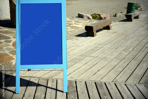 Blue blank advertising board on city street against wooden path with benches near caffee.