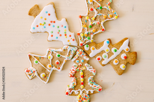 Five herringbone gingerbread cookies, differently decorated with glaze and sprinkles, set against a white painted wood texture.