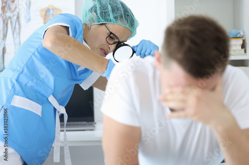 Practitioner doctor with magnifying glass in his hand examines rectum of man patient portrait. Protata cancer prevention annual medical check-ups concept.