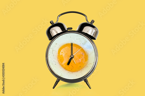 Fried egg sunny side on a vintage alarm clock on yellow background, surreal photo collage. Breakfast time concept