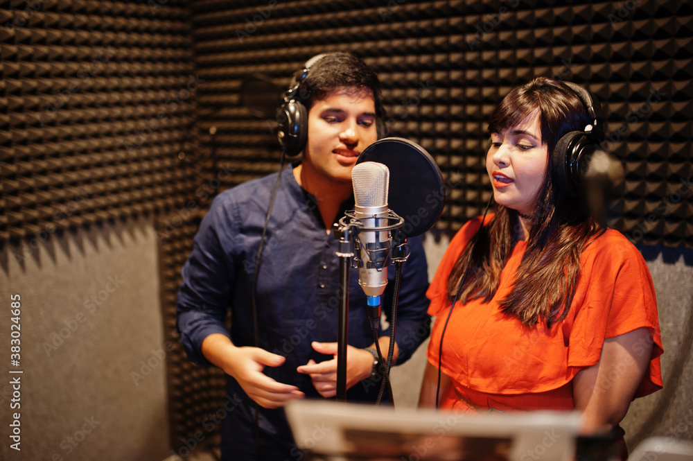 Young asian duet singers with microphone recording song in record music studio.