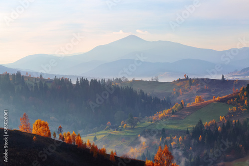 Amazing autumn scenery. Landscape with high mountains, fields and forests covered with morning fog. The lawn is enlightened by the sun rays. Touristic place Carpathians, Ukraine, Europe.