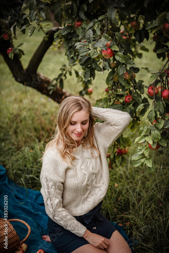 Cozy autumn portrait of blonde woman wearing a sweater on a warm autumn evening in an orchad