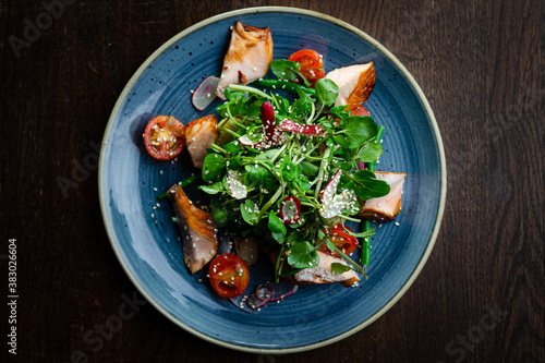 Kiln roast salmon salad with watercress, cherry tomatoes, radishes and sesame seeds on a blue plate top view