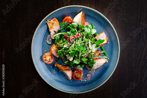 Kiln roast salmon salad with watercress, cherry tomatoes, radishes and sesame seeds on a blue plate top view
