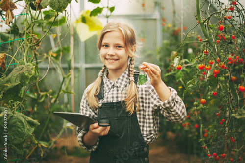 A beautiful little teenage girl with a tablet in her hands examines a sample of a plant through a magnifying glass. Curious children. Organic pure products