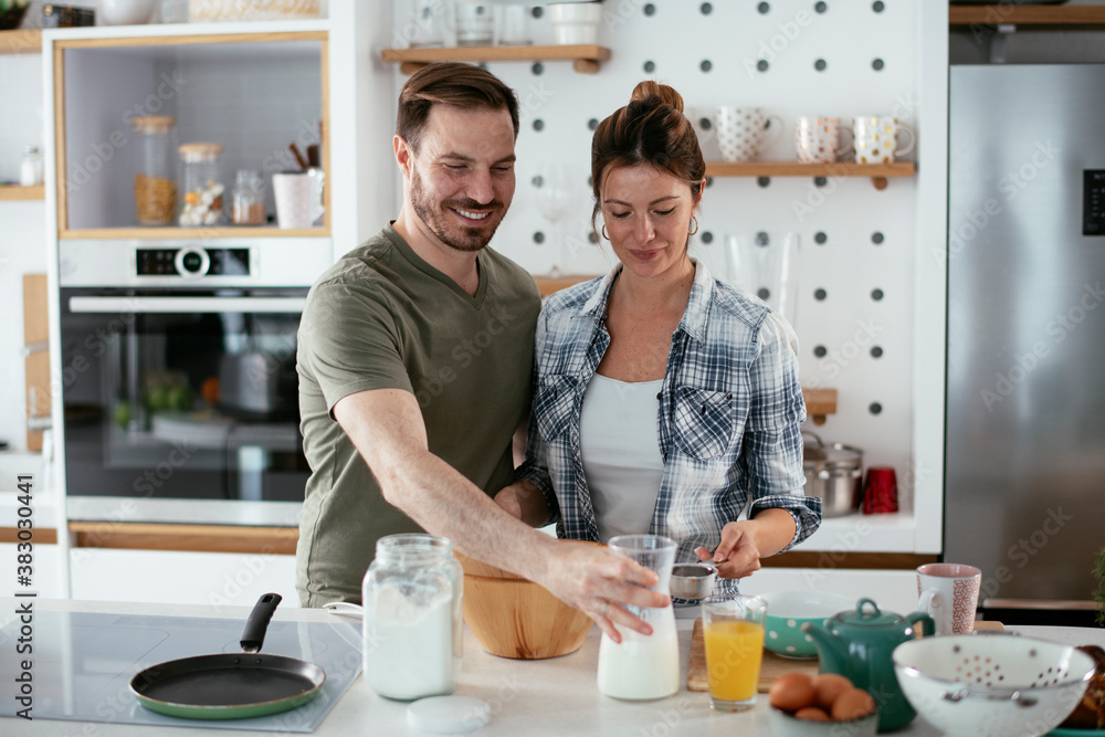Young couple making pancakes at home. Loving couple having fun while cooking.. Young couple making pancakes at home. Loving couple having fun while cooking..