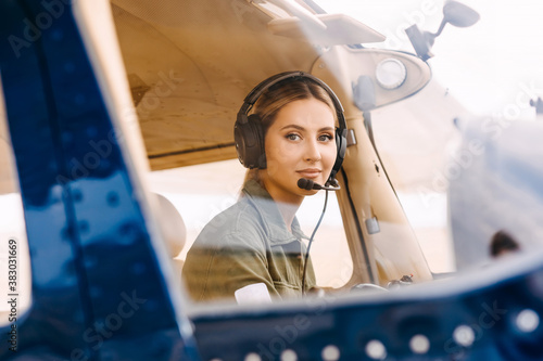 Fototapete Woman pilot sitting in airplane cockpit, wearing headset, looking at camera, smiling