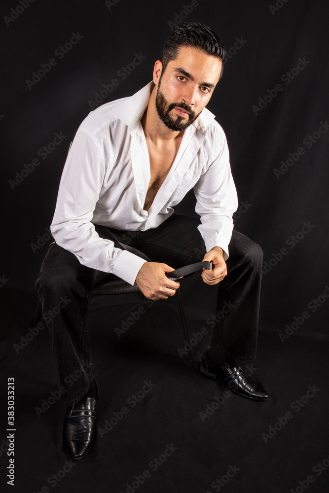 Handsome seductive dominant man with open shirt showing chest sitting on a chair. Attractive stylish bearded man in formal wear. Black background. Handsome seductive dominant man with open shirt showing chest sitting on a chair. Attractive stylish bearded man in formal wear. Black background.