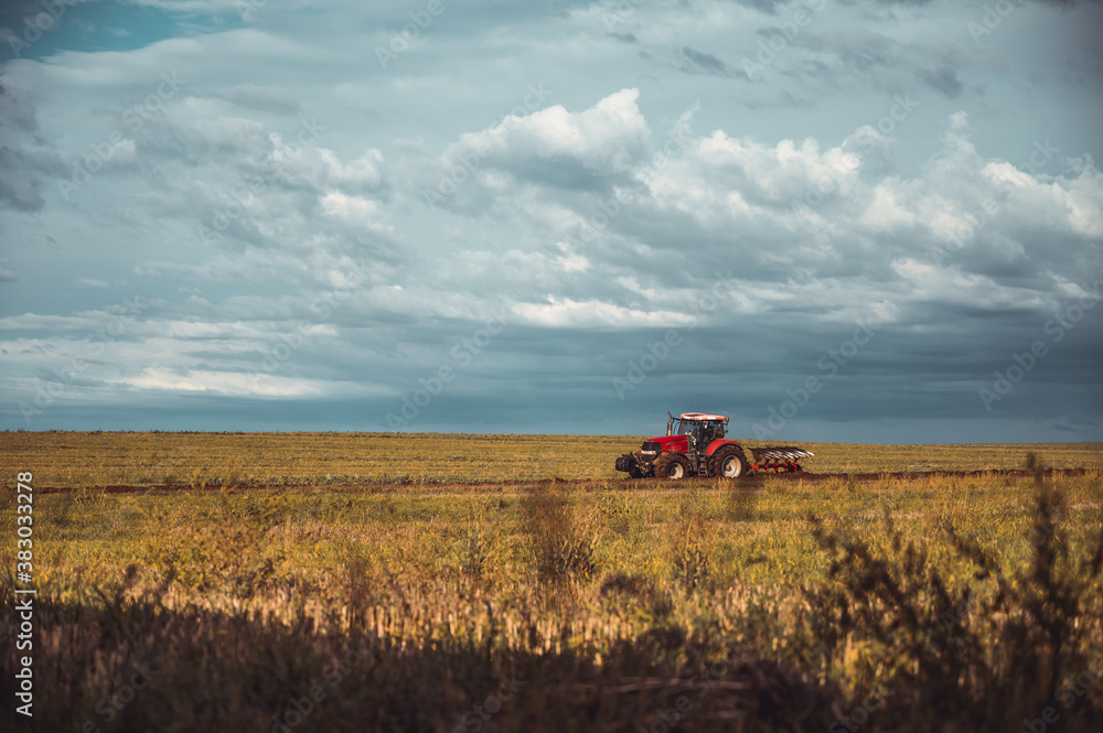 Fototapeta premium Tractor plowing the fields in the countryside. Agricultural tractor plowing the field. Red Tractor with plow.