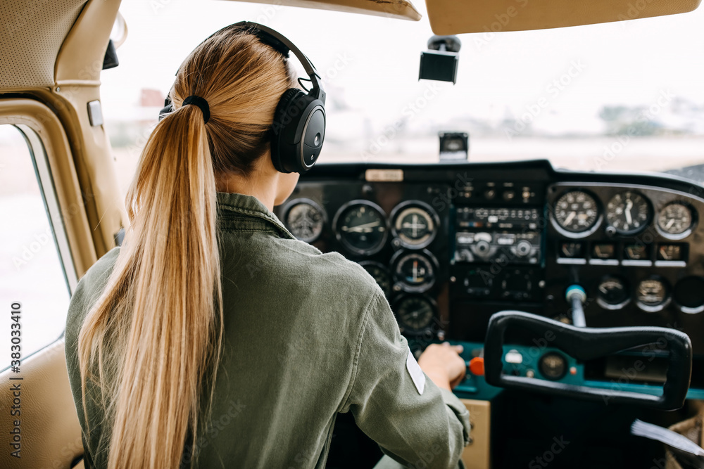 Back view over woman pilot flying an airplane, wearing headset. - obrazy, fototapety, plakaty 