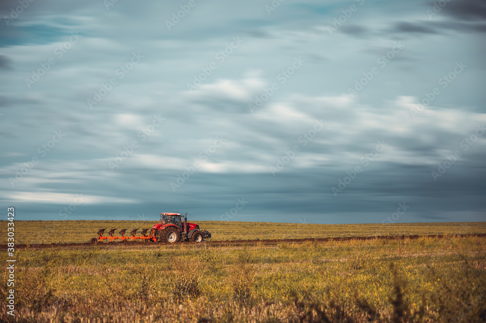 Fototapeta premium Tractor plowing the fields in the countryside. Agricultural tractor plowing the field. Red Tractor with plow.