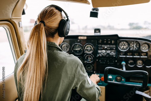 Fotografia Back view over woman pilot flying an airplane, wearing headset.