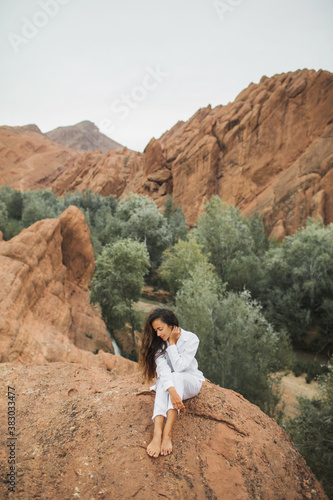 Pretty brunette woman in white sitting and enjoying view of Todra gorge canyon in Morocco. Harmony with nature and freedom concept. Travel lifestyle. © Oleg Breslavtsev