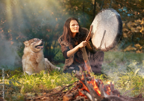 Billede på lærred Shaman woman drumming in the sunny forest with an Alaskan Malamute dog