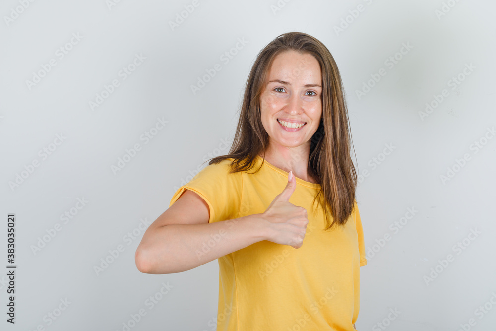 Young woman in yellow t-shirt showing thumb up and looking cheerful , front view. Young woman in yellow t-shirt showing thumb up and looking cheerful , front view.