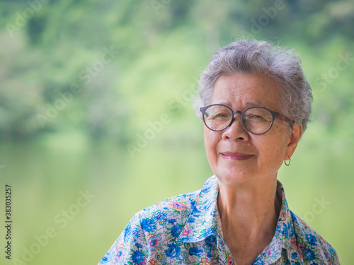 A portrait of an elderly Asian woman smiling and looking at camera while standing in the park. Concept of old people and healthcare