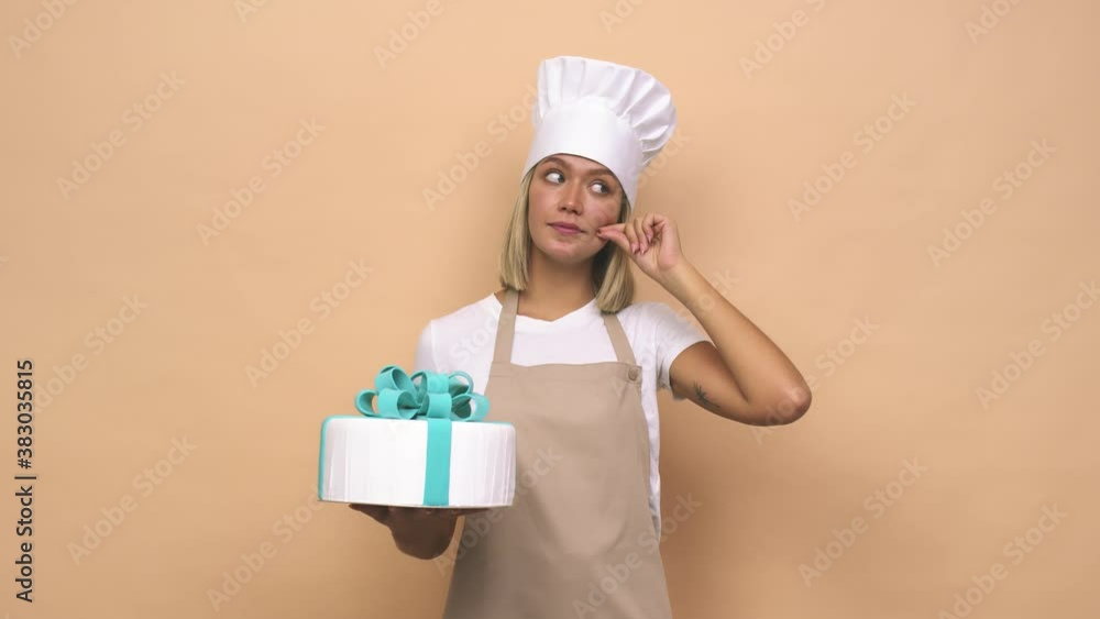 Young cook woman holding a cake with fingers on lips keeping a secret Young cook woman holding a cake with fingers on lips keeping a secret